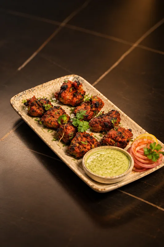 Grilled chicken kebab pieces on a platter with green chutney and onion