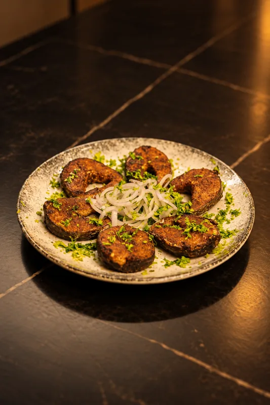 Plate of masala fish fry slices with sliced onion and coriander